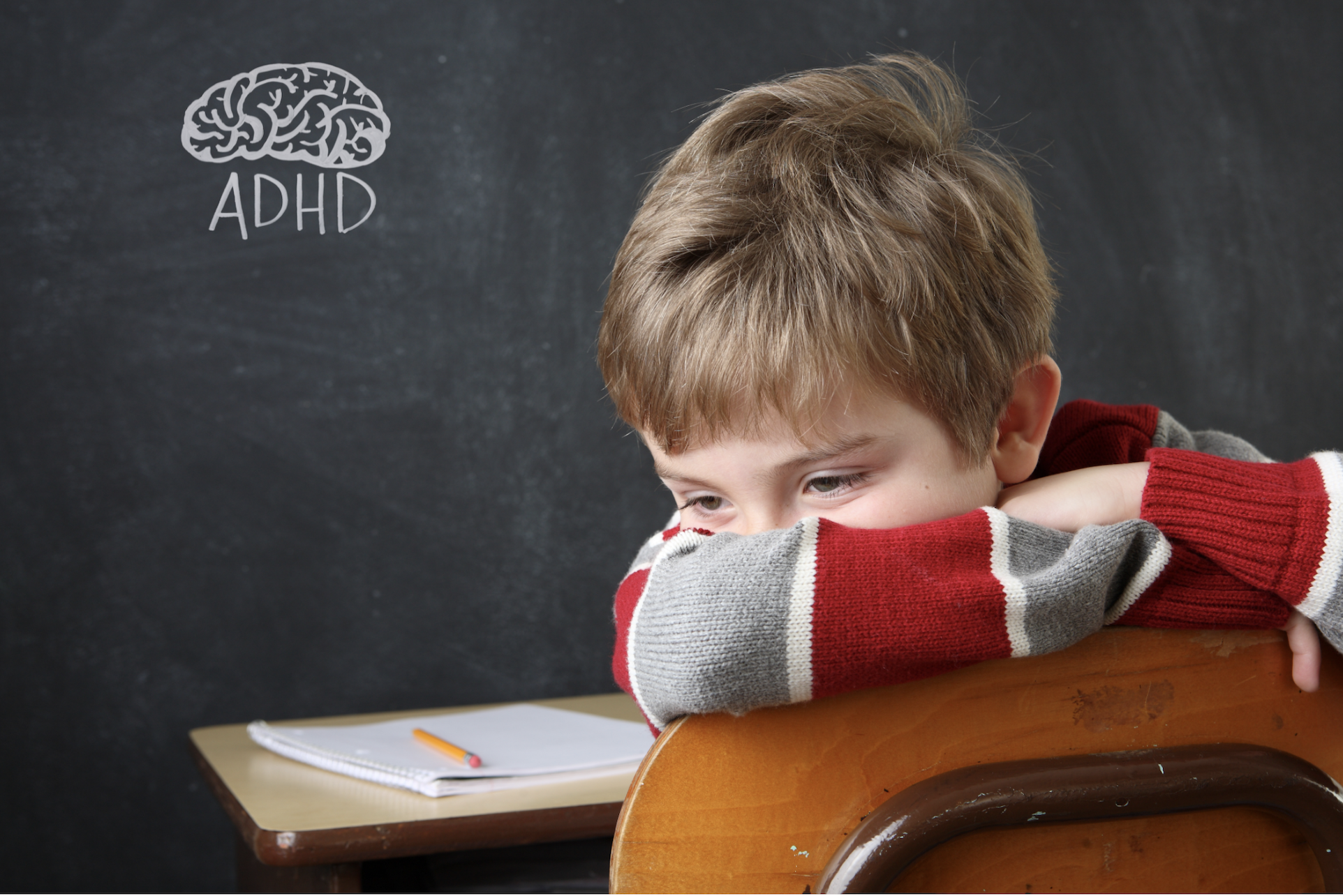 A bored child in the classroom turning his back against the chalk board.